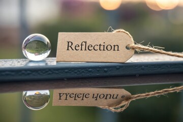 Close-Up of a Glass Sphere with a Tag Reading 'Reflection' Resting on a Calm Surface Surrounded by a Soft Bokeh Background