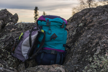 teal and purple hiking backpack resting on rugged rocks with another grey pack in background, representing outdoor exploration, trekking, and wilderness adventure in nature. close up.