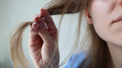 Close up of a woman holding dry hair ends. Concept of hair damage, split ends, hair care and treatment. Natural blonde hair, hand with manicured nails. Hair health and beauty problem. Caucasian woman.