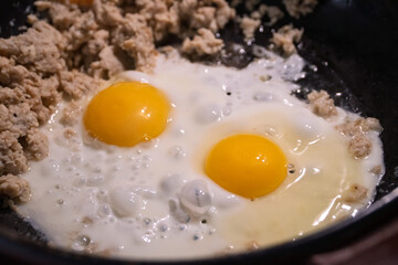 Cooking fried eggs with minced meat for breakfast. Cooking scrambled eggs for quick, nutritious breakfast before work. The concept of food consumption. Frying chicken eggs in a black skillet. 