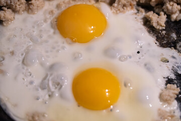 Cooking fried eggs with minced meat for breakfast. Cooking scrambled eggs for quick, nutritious breakfast before work. The concept of food consumption. Frying chicken eggs in a black skillet. 
