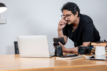 A young male freelance photographer enjoys working from home, surrounded by his camera and creative setup.