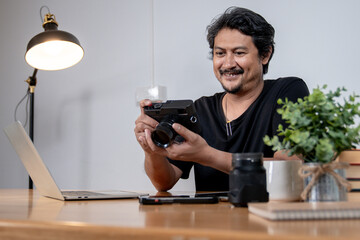 A young male freelance photographer enjoys working from home, surrounded by his camera and creative setup.