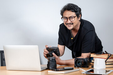 A young male freelance photographer enjoys working from home, surrounded by his camera and creative setup.