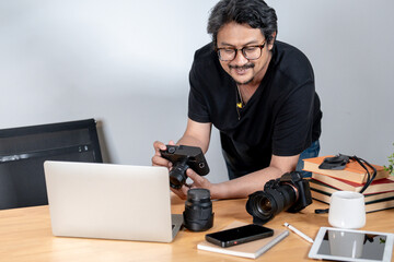 A young male freelance photographer enjoys working from home, surrounded by his camera and creative setup.