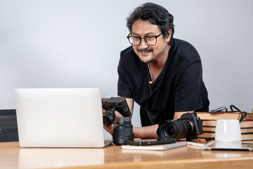A young male freelance photographer enjoys working from home, surrounded by his camera and creative setup.