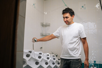 Obraz premium Male gardener watering leafy plants growing vertically in bathroom hydroponic setup, demonstrating urban agriculture and water-efficient home cultivation techniques. Concept of home gardening.