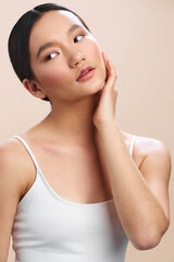 Asian woman with a serene expression rests her face on her hand against a light backdrop, conveying...