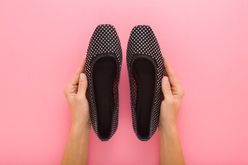 Young adult woman hands holding and showing new dark black casual summer shoes on light pink table background. Pastel color. Closeup. Female footwear. Point of view shot. Top down view.