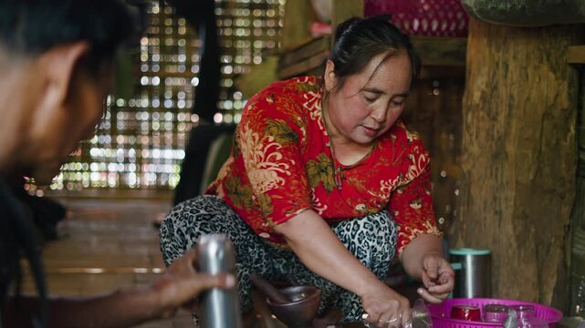 A lahu woman from Southeast Asia prepares spices for traditional food on the ground inside a wooden house