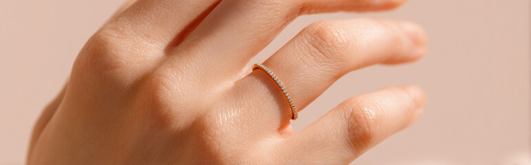 Fototapeta premium Close-Up of Elegant Female Hand Wearing Gold Double Ring on Soft Pink Background