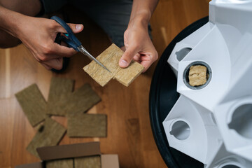 Close-up top view of gardener hands cutting rockwool with scissors, preparing hydroponic media for seed starting, highlighting precision in indoor cultivation techniques. Concept of home gardening.