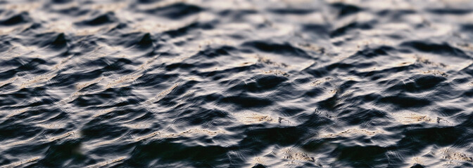 A detailed, wide-format shot of dark, rippling water with a choppy surface, resembling deep ocean...