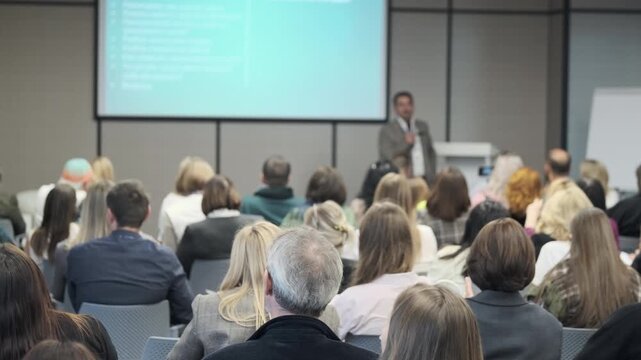 Professional speaker delivers presentation to engaged audience in a conference setting, highlighting learning and collaboration in a modern seminar hall.