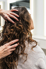 Naklejka premium Professional hands styling and caring for a woman's long, brown, curly hair during a treatment in a modern beauty salon