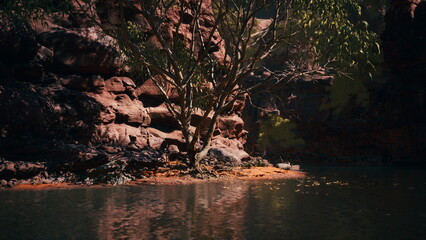 A calm body of water reflects the stunning red cliffs and lush greenery surrounding it. The tranquility of nature offers a peaceful escape into the wilderness, evoking a sense of harmony.