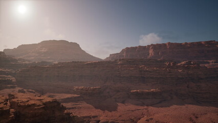 Deep canyons rise dramatically under the warm sunlight, casting shadows on rocky formations. The serene atmosphere invites exploration and adventure through the rugged terrain.