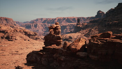 A breathtaking landscape showcases towering red rock formations framed by rugged canyon walls, illuminated by the bright midday sun in a remote desert location.