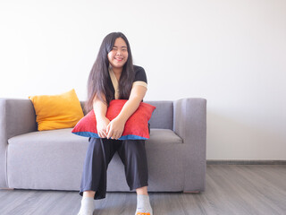 Young woman sits on sofa hugging cushion, smiling and relaxing. Simple pleasures at home concept.