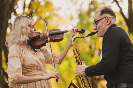 Beautiful blonde violinist and saxophonist perform melodies in autumn park. Fantastic romantic mood, a touch of autumn. Musical instruments  playing at an outdoor concert. A musical duet. Portrait