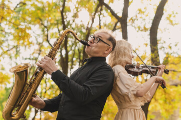 Beautiful blonde violinist and saxophonist perform melodies in autumn park. Fantastic romantic mood, a touch of autumn. Musical instruments  playing at an outdoor concert. A musical duet. Portrait