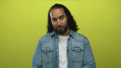 Man with beard looking at camera wearing denim jacket and white tee in lime green studio; confident presence.