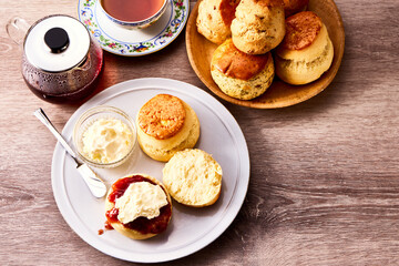 紅茶とともに楽しむアフタヌーンティーのスコーン。クロテッドクリームとジャムを添えて味わう伝統的な英国風ティータイムの一場面。ティーポットやカップと共に並べられたスコーンは、洋菓子、デザート、カフェ、休日のひとときを表現する素材写真として利用可能。