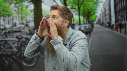 Bearded man holds hand in phone gesture to ear on a busy city street next to rental bike racks...