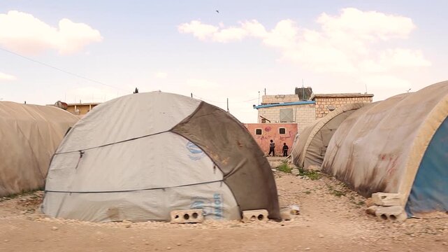 Refugee tents blend with village houses in northern Aleppo, Syria, symbolizing the urgent need for reconstruction and international aid after years of war. Documentary on recovery and humanity.
