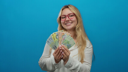 Young woman with glasses holding romanian lei banknotes smiling against a vibrant blue background...