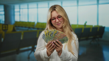 Young woman in airport terminal counting romanian lei banknotes, expressing financial planning or...