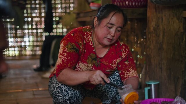 Lahu woman cooking and grinding traditional spices in a rustic wooden kitchen wearing red shirt while preparing authentic local cuisine