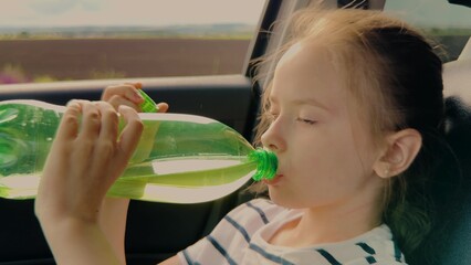 Thirsty child drinking water in the car, Girl quenches her thirst during a road trip, Summer travel...