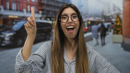 Woman wearing striped shirt with glasses pointing finger upward in busy street; surprise discovery...