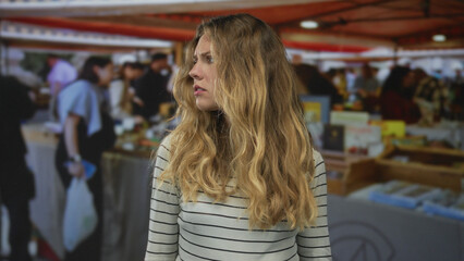 Fototapeta premium Woman face looking at market stalls shows blonde young figure with wavy striped top and a concerned expression blending into the crowd.