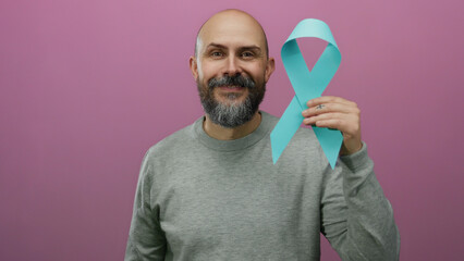 Man with beard holding blue awareness ribbon against isolated pink background confidently posing...