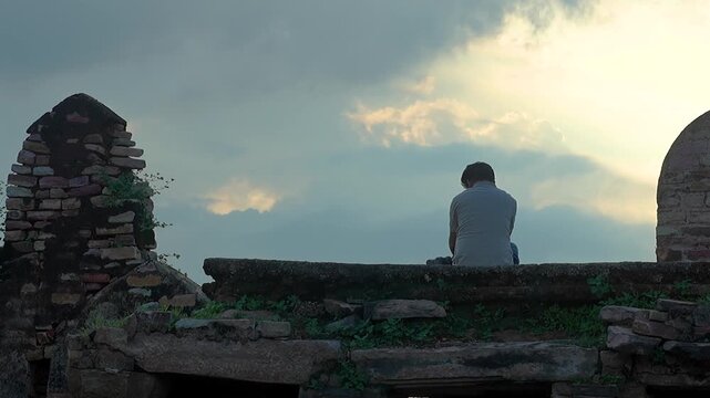 isolated young man sitting at stone at an old fort wall in India