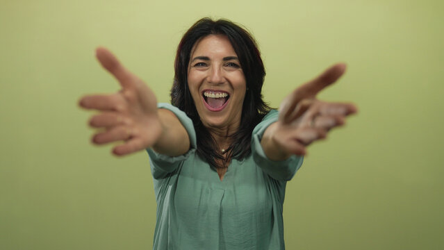 Fototapeta Hispanic woman with broad smile extends bare arms forward for hug gesture in green studio  affection.