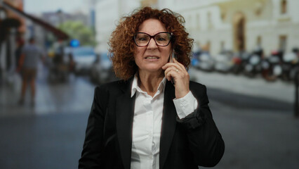Woman talking on cellphone in city street wearing glasses and black jacket with blurred background...