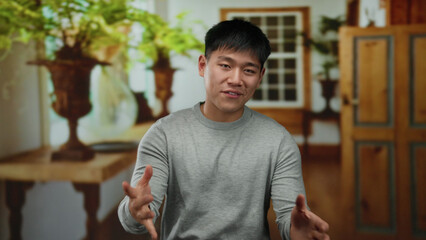 Young chinese man standing indoors in a cozy hotel room with wooden decor and plants, creating a...