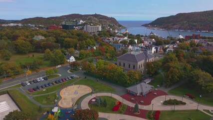 A sweeping aerial view over St. John's Newfoundland in autumn reveals a coastal park with winding paths, colourful homes on the hillside and the harbour stretching out under clear skies. - Powered by Adobe