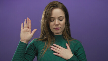 Young caucasian woman holds hand to chest and raises palm in studio setting, wearing green sweater...