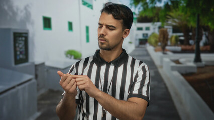 Young hispanic male referee counting with fingers in an urban outdoor city street, showcasing his...