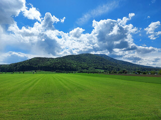 landscape with emerald field and dark green Pohorje mountain under blue sky. Slovenia.
