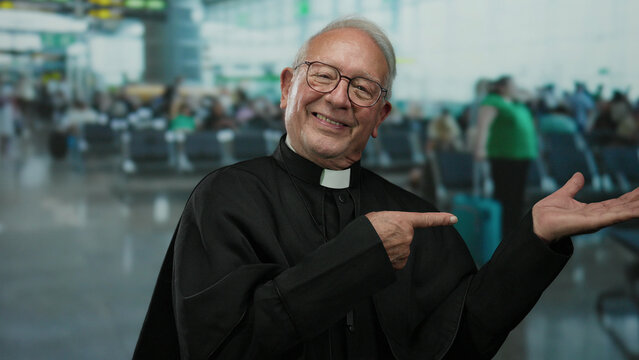 Senior priest in black robe smiling and pointing in busy airport terminal backdrop with blurred travelers and seating.