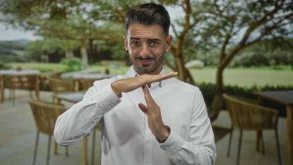 Young smiling man in white shirt making time out gesture with hands in building; pause calm focus...