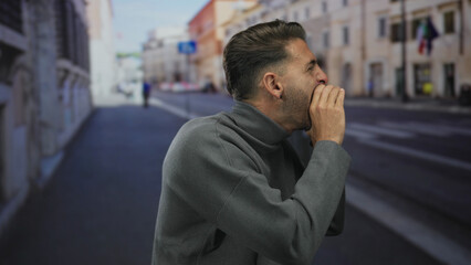 Obraz premium Young hispanic man cups hands around mouth shouting on busy urban street lined with buildings; public alert urgency.
