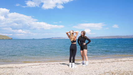 Two women enjoying a sunny day at Lake Baikal's scenic shoreline in athletic wear