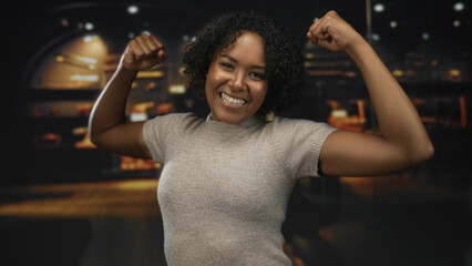 Young african american woman wearing grey sweater flex arms and raise fists in building; confidence...
