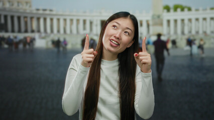 Fototapeta premium Woman smiling in the vatican's st. peter's square points upward, capturing a joyful moment amid a bustling urban cityscape.